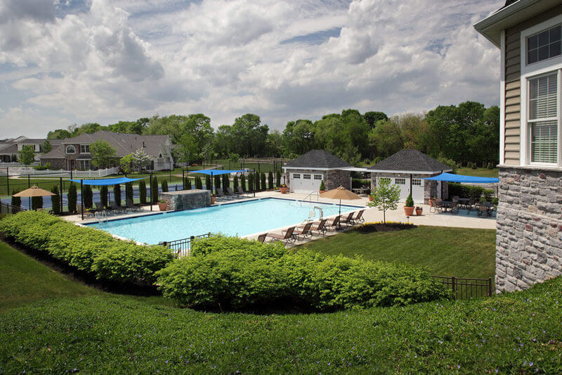 Large pool surrounded by lounge chairs with a tennis court in the background