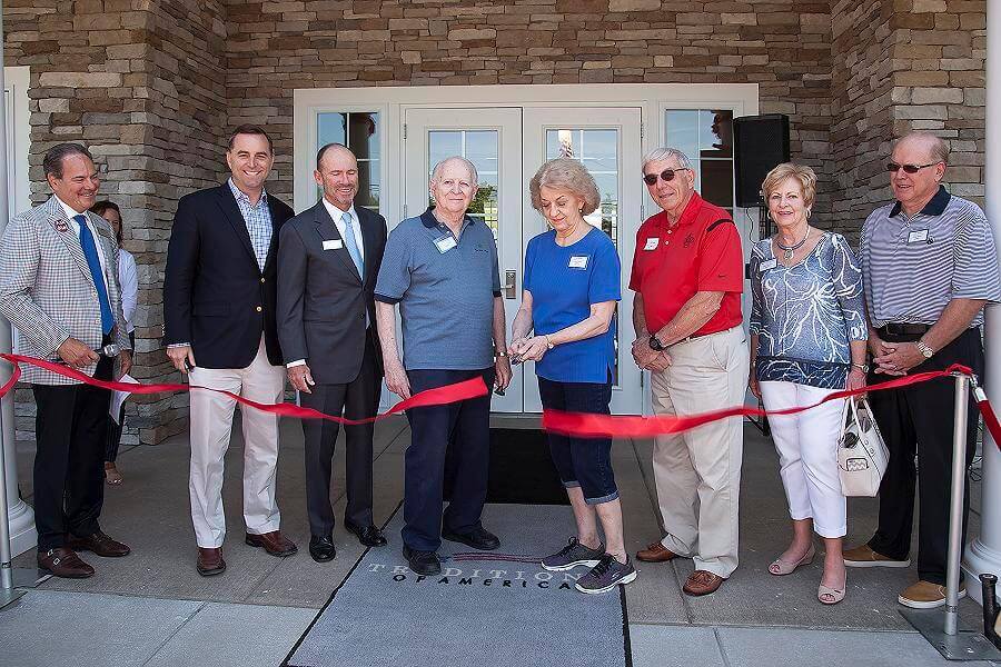 People cutting the ribbon in front of a traditions of America community clubhouse