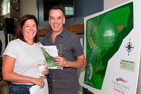 Two people standing in front of the Traditions of America community plat map