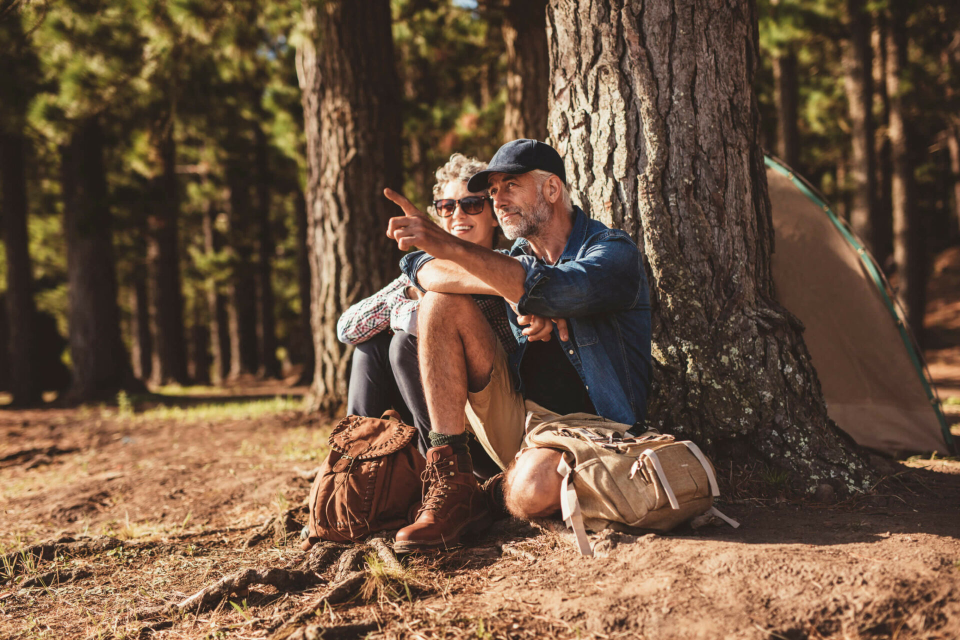 Portrait of mature couple relaxing at their campsite with man showing something to woman. Senior couple hiking and camping in forest on a summer day.