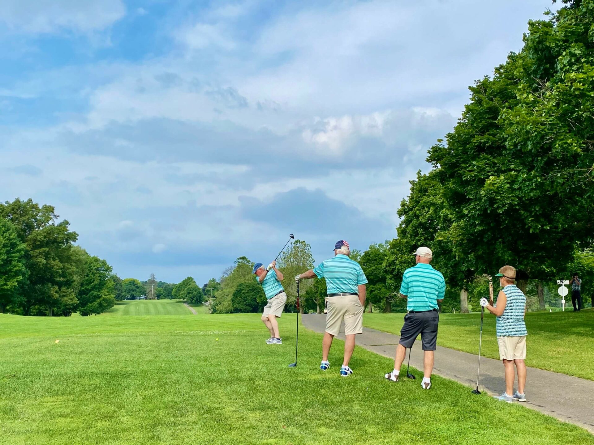 Person teeing off with three others watching on a golf course