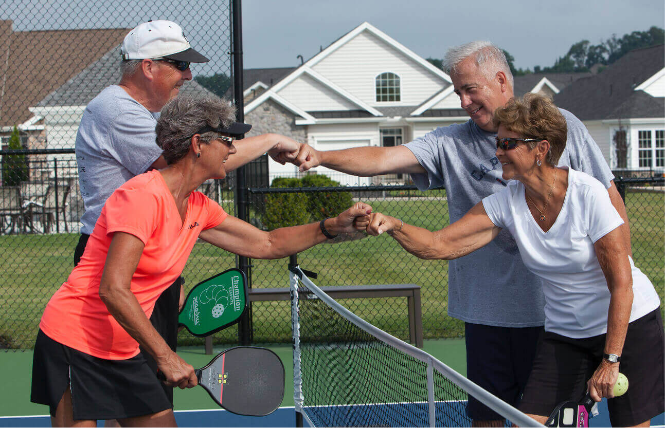 People fist bumping over a pickle ball net
