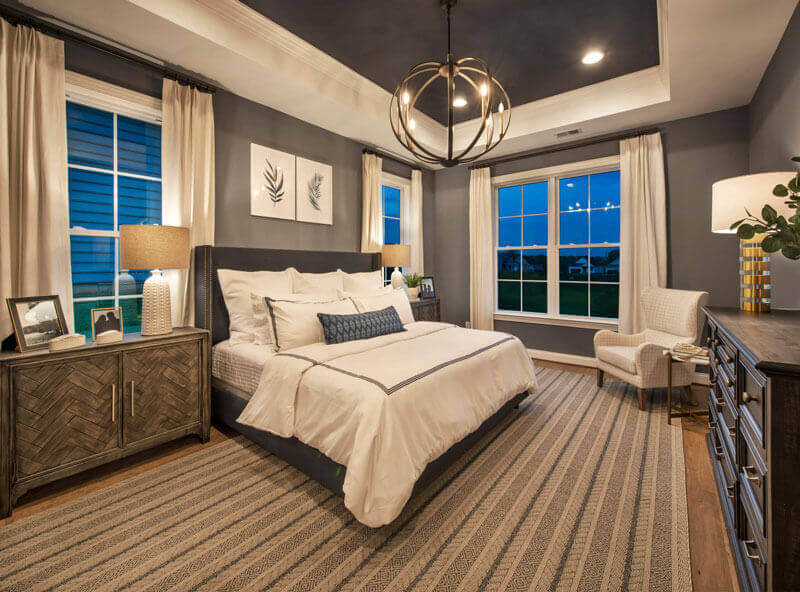 The Grant Primary Bedroom with grey walls a chandelier and bed in the center
